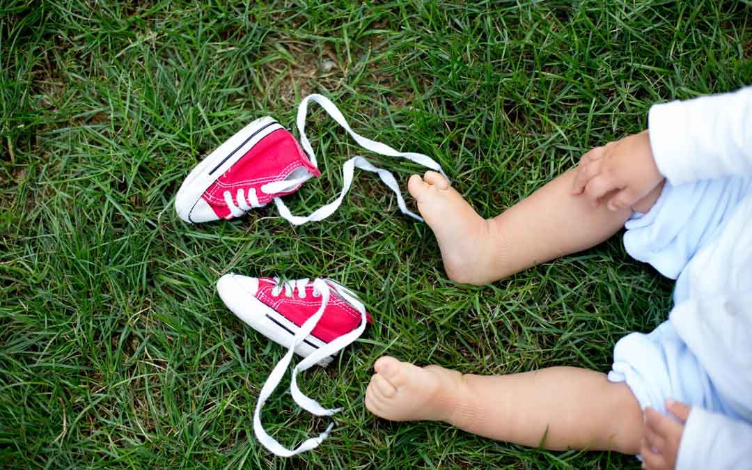 barefoot baby sitting on lawn with red shoes