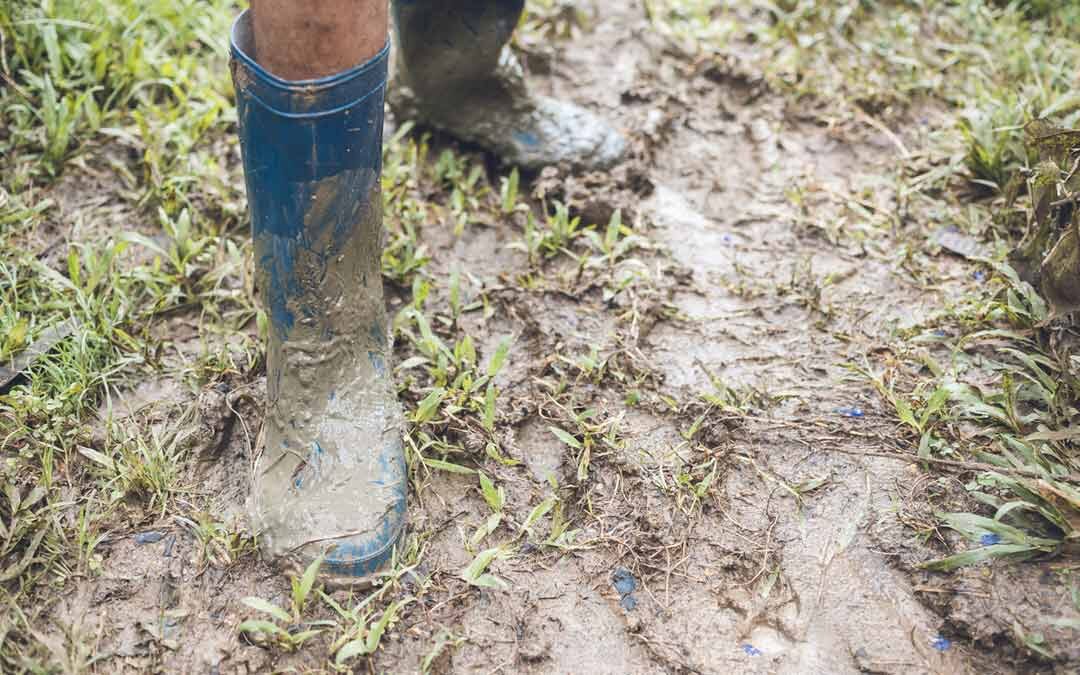 child in blue rubber rain boots standing in mud