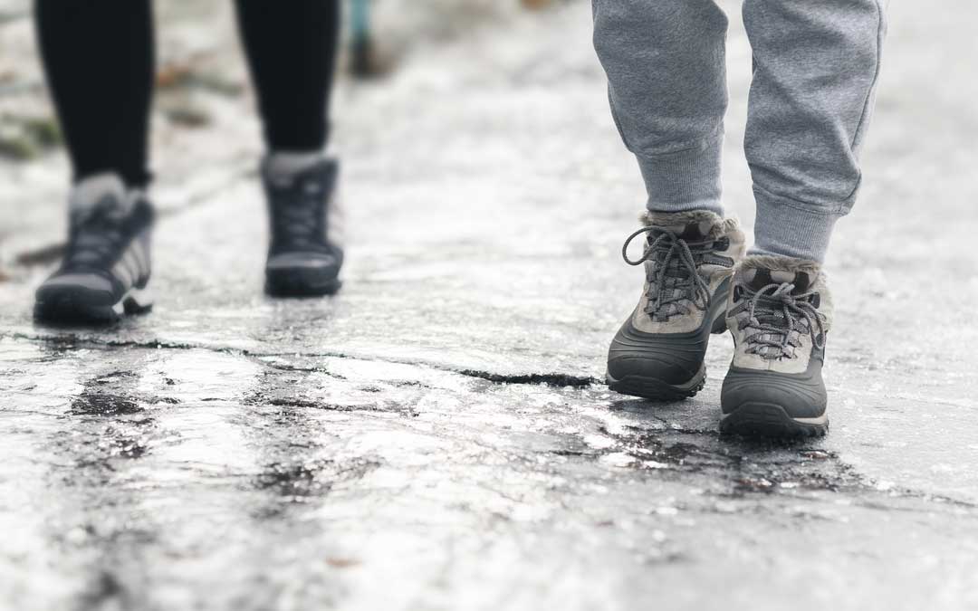 an closeup image of two pedestrians' feet walking on icy sidewalk